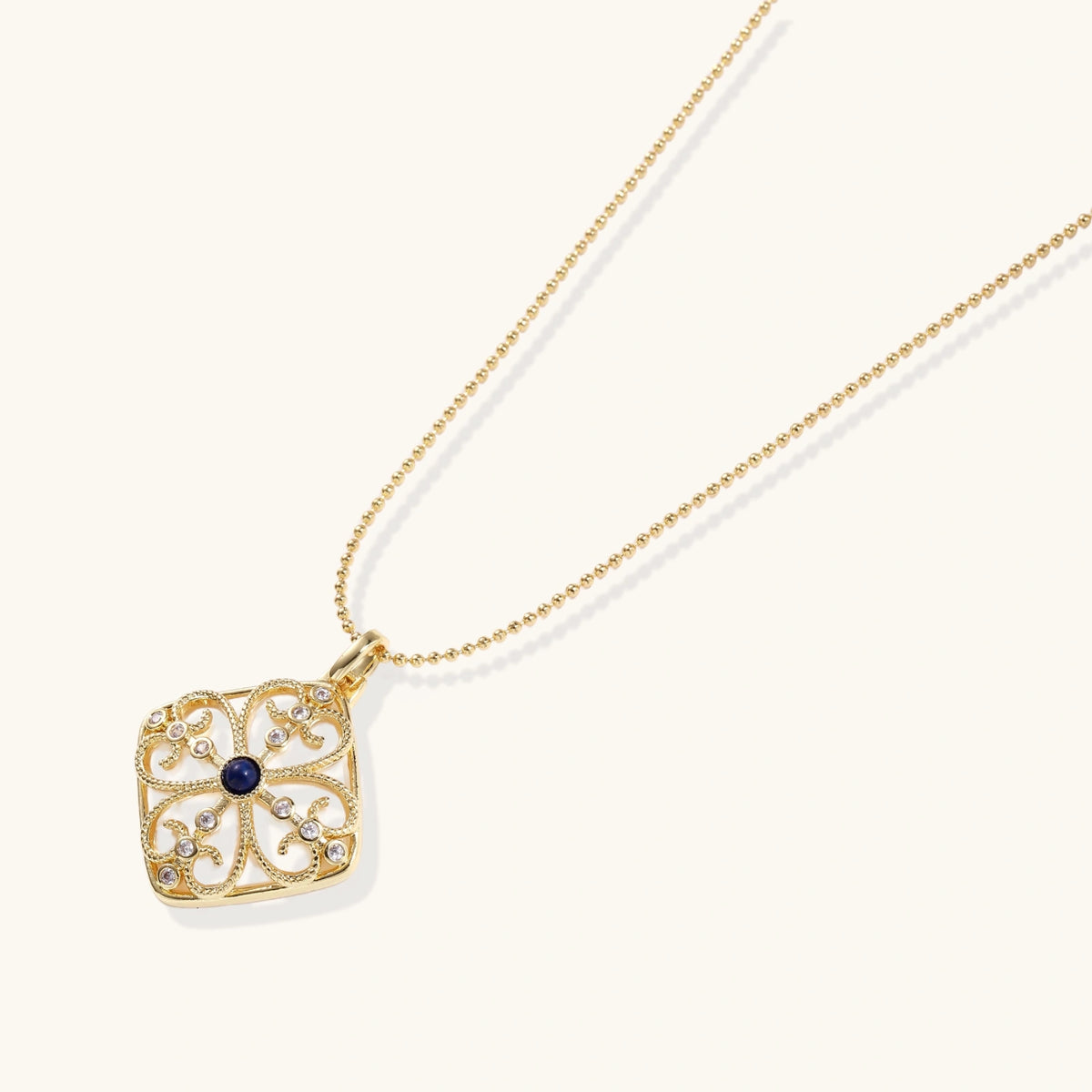 Gold filigree pendant with quatrefoil design, deep blue lapis lazuli center, clear crystal accents on ball chain