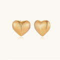 Gold heart-shaped stud earrings with parallel ridged texture on cream background