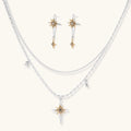 Layered silver-toned necklace set with cross pendant and gold sun charm detail, matching drop earrings on white background.